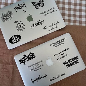 May include: Two silver laptop computers with various black and white stickers. The stickers include the words "Halsey", "Be Kind", "Nightmare", "Forever is a long time", "I'm tired and angry, but somebody should be", "You can find me in the kingdom", "Well be looking for sunlight", "Don't belong to no city. Don't belong to no man", "Hopeless", "Without me", and "These violent delights have violent ends".