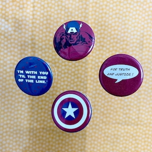 Könnte beinhalten: Vier runde Anstecknadeln mit rot-weiß-blauen Farbschemata. Eine Nadel zeigt ein Cartoon-Bild von Captain America mit dem Text "A". Eine weitere Nadel zeigt den Text "I'M WITH YOU 'TIL THE END OF THE LINE.". Eine dritte Nadel zeigt den Text "FOR TRUTH AND JUSTICE!". Die vierte Nadel zeigt einen Stern mit einem rot-weiß-blauen Farbschema.