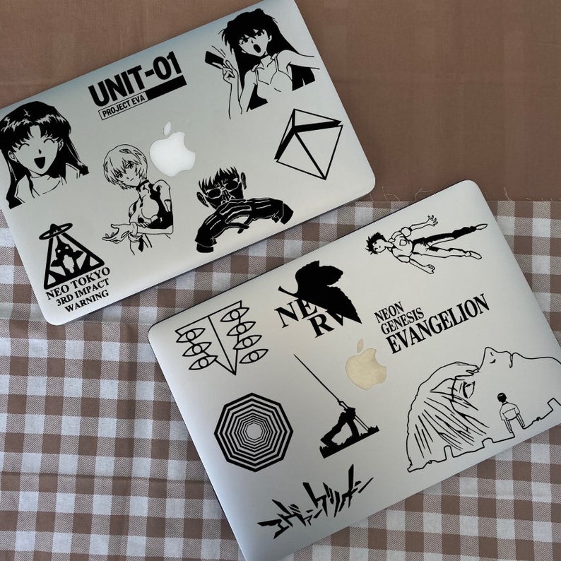 Pu&ograve; includere: Due laptop argentati con adesivi in ​​bianco e nero con personaggi e testo della serie anime Neon Genesis Evangelion. Gli adesivi includono il testo "UNIT-01", "PROJECT EVA", "NEO TOKYO", "3RD IMPACT", "WARNING", "NE", "R", "NEON GENESIS", "EVANGELION", e "エヴァンゲリオン".
