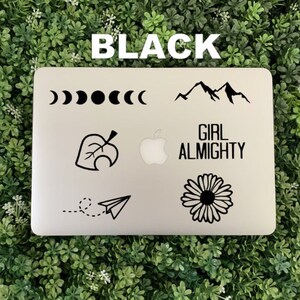 Pu&ograve; includere: Un laptop bianco con adesivi neri. Gli adesivi includono una catena montuosa, una foglia, una mezzaluna, una margherita, un aeroplano di carta e il testo "Girl Almighty".