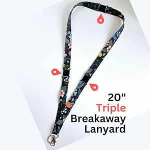 May include: A 50.8 cm triple breakaway lanyard featuring a dark navy blue fabric strap with a repeating pattern of orange citrus fruits, green leaves, and small white flowers. The lanyard includes three black plastic safety release buckles.