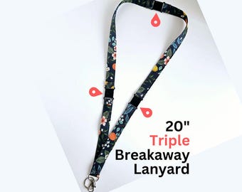 May include: A 20" triple breakaway lanyard featuring a dark fabric strap with a repeating pattern of orange fruit, green leaves, and small white flowers. The lanyard includes three black plastic breakaway clasps and a metal split ring at the end.