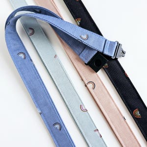 May include: Four fabric lanyards featuring a repeating rainbow pattern. The lanyards come in blue, light blue, light pink, and black. Each strap includes a black plastic buckle and a black plastic connector for attaching items securely to the fabric.
