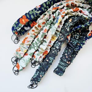 May include: A collection of floral patterned straps with metal clasps. The straps feature various designs, including orange and white flowers on a navy background, and a white background with green leaves and pink flowers.