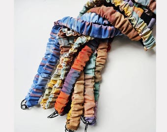 May include: A collection of fabric-covered elastic lanyards featuring a variety of plaid and solid-colored patterns in shades of blue, orange, yellow, and tan. Each lanyard is gathered with a scrunchie-style texture and includes a metal clasp.