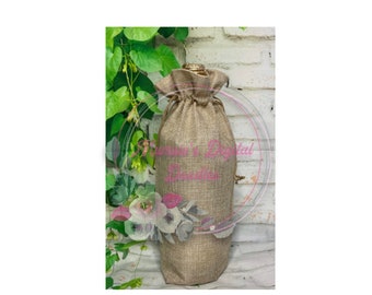 May include: A brown burlap bottle bag with a drawstring closure. The bag is sitting on a white brick wall with green vines in the background.