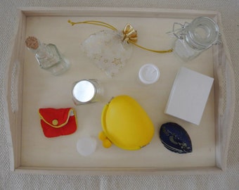 May include: A wooden tray with a variety of small items, including a clear glass bottle, a small white pouch with gold stars, a yellow pouch, a red pouch, a small white jar, a small white container, a clear glass jar with a silver lid, and a blue pouch with a white design.