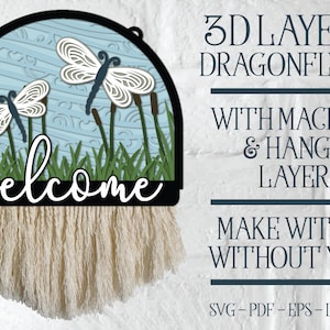 May include: A 3D layered dragonfly welcome sign with a macrame hanger. The sign is made of wood and features two dragonflies, reeds, and grass. The sign is painted in shades of blue, green, and white. The sign says "welcome" in black cursive lettering. The sign can be made with or without yarn.