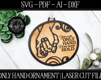 Op de afbeelding: Een lasergesneden houten ornament in de vorm van twee handen die elkaar vasthouden. Het ornament is bruin met zwarte letters die "Yours is the ONLY HAND I'll ever need to HOLD" lezen.