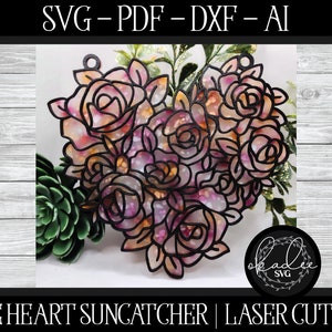 May include: A black and white digital design of a heart-shaped rose bouquet. The roses are in shades of pink and orange. The design is labeled "ROSE HEART SUNCATCHER | LASER CUT FILE" and "okaddie SVG".