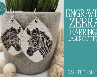 May include: A pair of laser cut wooden earrings featuring a black and white zebra design. The earrings are engraved with a zebra head and are ready to be assembled.  The text "ENGRAVED ZEBRA EARRINGS LASER CUT FILE SVG-PDF-AI-DXF" is displayed on a teal background.