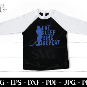 以下が含まれることがあります： 黒と白のラグランスリーブTシャツに、青いホッケー選手のシルエットと「Eat Sleep Rink Repeat」という青いテキストが書かれています。