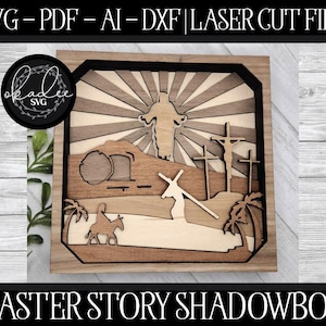 May include: A wooden shadow box with a laser cut design depicting the Easter story. The scene includes Jesus on the cross, the empty tomb, and a figure carrying a cross. The box is framed in dark wood and has a light wood background.