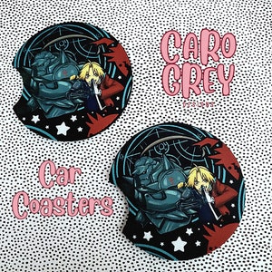 May include: Two black and red round car coasters with a white star design. The coasters feature a cartoon image of a character from the anime Fullmetal Alchemist. The text "CARO GREY DESIGNS" is printed in pink on the top coaster.