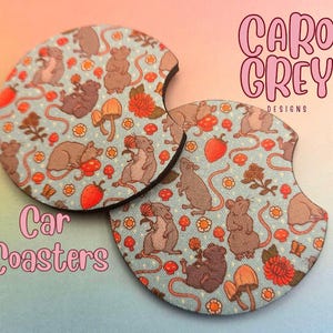 May include: Two round car coasters with a blue background and a pattern of mice, flowers, and mushrooms. The text "Caro Grey Designs" is printed on the top coaster.