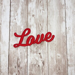 May include: A red embroidered patch with the word "Love" in a cursive script. The patch is set against a light brown and white wood grain background.
