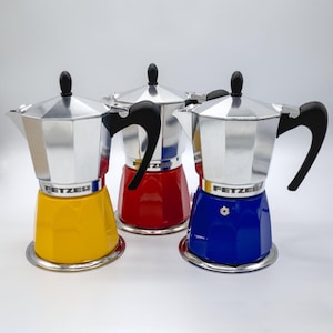 Peut inclure: Trois cafetières à piston en argent avec des poignées noires. Le fond de chaque cafetière est d'une couleur différente : jaune, rouge et bleu. Chaque cafetière porte l'inscription "FETZER" sur le côté.