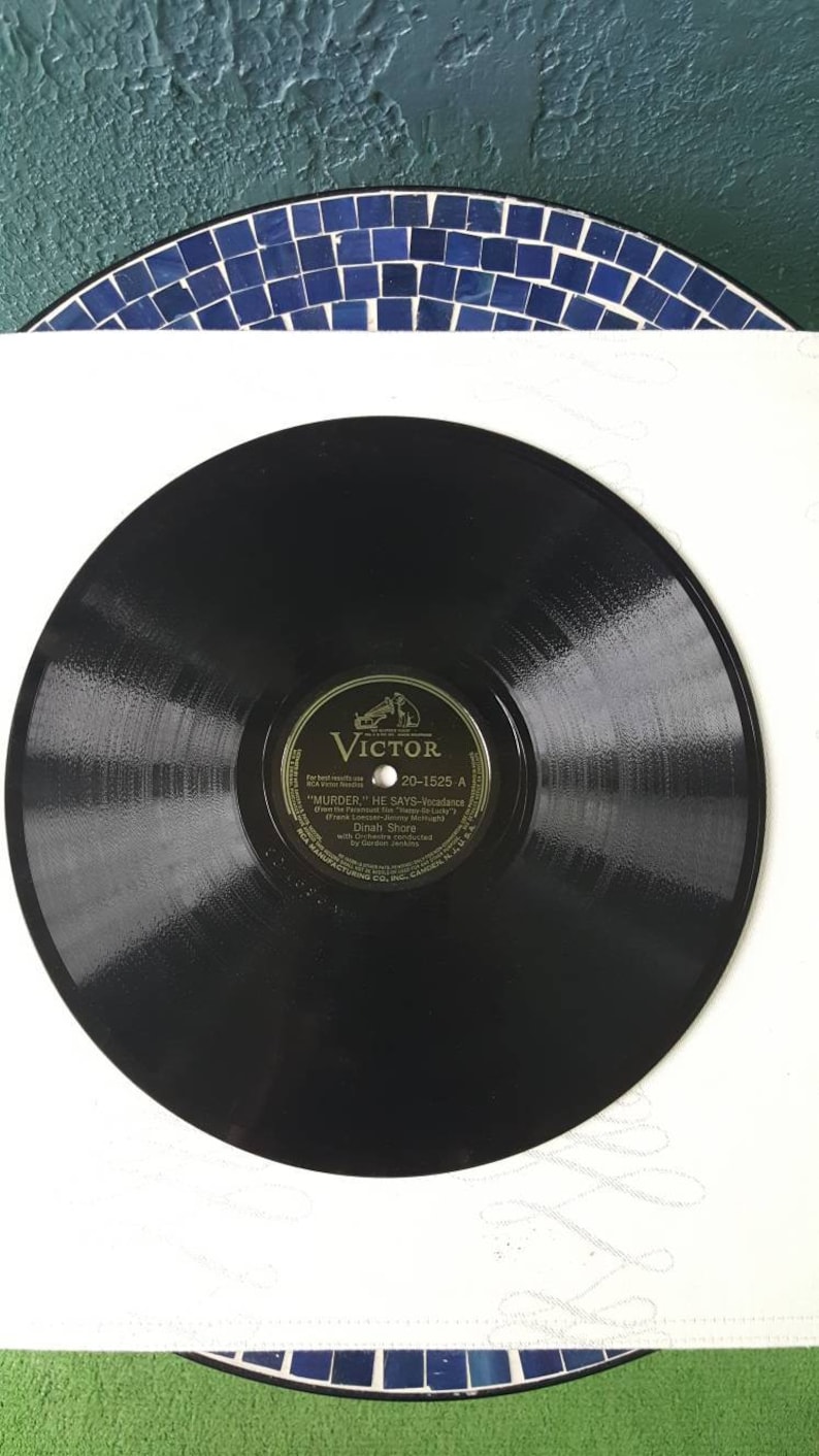 May include: A black vinyl record with a gold label. The label has the text "Victor" and "20-1525 A" and the song title "Murder He Says - Vocalese" by Dinah Shore.
