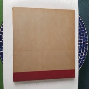 May include: A tan hardback book with a red spine. The book is lying flat on a white surface.