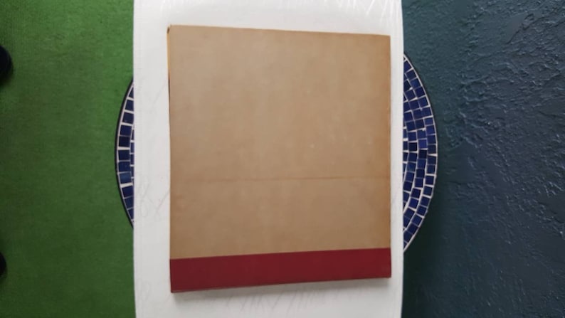 May include: A tan hardback book with a red spine. The book is lying flat on a white surface.