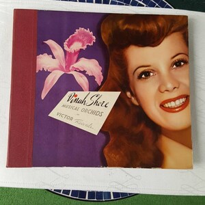 May include: A vintage vinyl record album cover featuring Dinah Shore with a pink orchid and the text "Dinah Shore Musical Orchids on Victor Records".