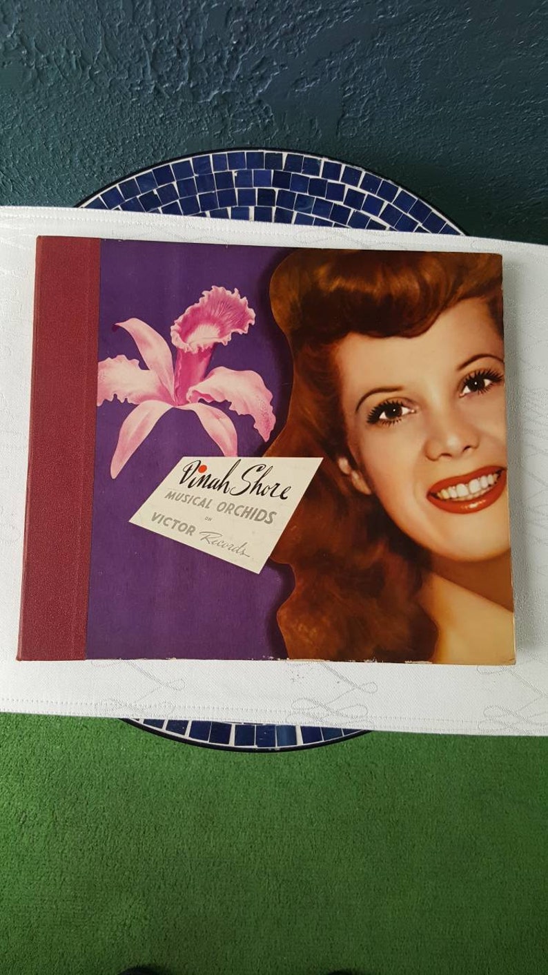 May include: A vintage vinyl record album cover featuring Dinah Shore with a pink orchid and the text "Dinah Shore Musical Orchids on Victor Records".