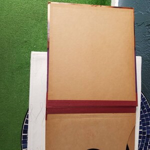 May include: A brown cardboard box with a burgundy trim. The box is closed and has a flap on the top.