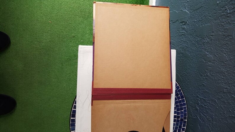 May include: A brown cardboard box with a burgundy trim. The box is closed and has a flap on the top.