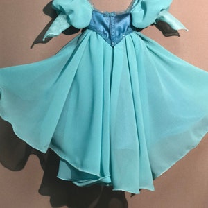 Op de afbeelding: Een lichtblauwe jurk met een zwierige rok en pofmouwen. Het lijfje is een donkerdere tint blauw met pailletten. De jurk lijkt gemaakt van een lichte, transparante stof, geschikt voor een kostuum of speciale gelegenheid.