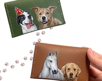May include: Two leather cardholders featuring hand-painted pet portraits. One is olive green with a dog wearing a party hat and another dog. The other is brown with a white horse and a golden retriever. Paw prints are in the background.