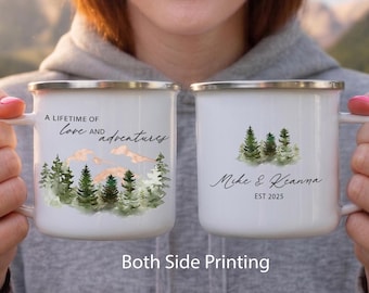 May include: Two white enamel mugs with silver rims. The left mug features a watercolor forest, mountains, and the text A LIFETIME OF LOVE AND adventures. The right mug displays a watercolor forest and the text Mike & Keanna EST 2025.