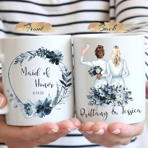 Może przedstawiać: Biały kubek ceramiczny z niebieskim wieńcem kwiatowym i tekstem "Maid of Honor 8.14.25". Tył kubka przedstawia niebieski wz&oacute;r kwiatowy z dwiema kobietami w białych sukienkach i tekstem "Brittany & Jessica".