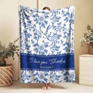 May include: A white and blue floral blanket with a blue border. The blanket features a floral pattern with birds and the text "I love you, Grandma" and the name "Charlotte".