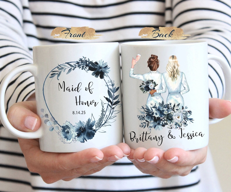 Może przedstawiać: Biały kubek ceramiczny z niebieskim wieńcem kwiatowym i tekstem "Maid of Honor 8.14.25". Tył kubka przedstawia niebieski wz&oacute;r kwiatowy z dwiema kobietami w białych sukienkach i tekstem "Brittany & Jessica".