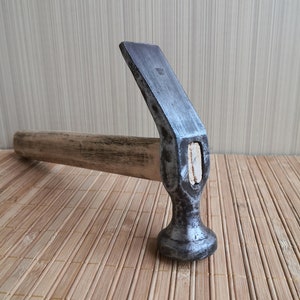 Puede incluir: Un martillo plateado con mango de madera, descansando sobre una estera de bambú.