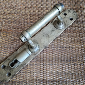 Puede incluir: Una manija de puerta plateada con una palanca larga y una cerradura. La manija está montada en una placa rectangular.