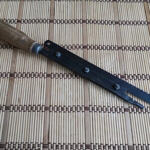 May include: A black metal saw with a wooden handle. The saw has a serrated blade and is attached to the handle with screws.