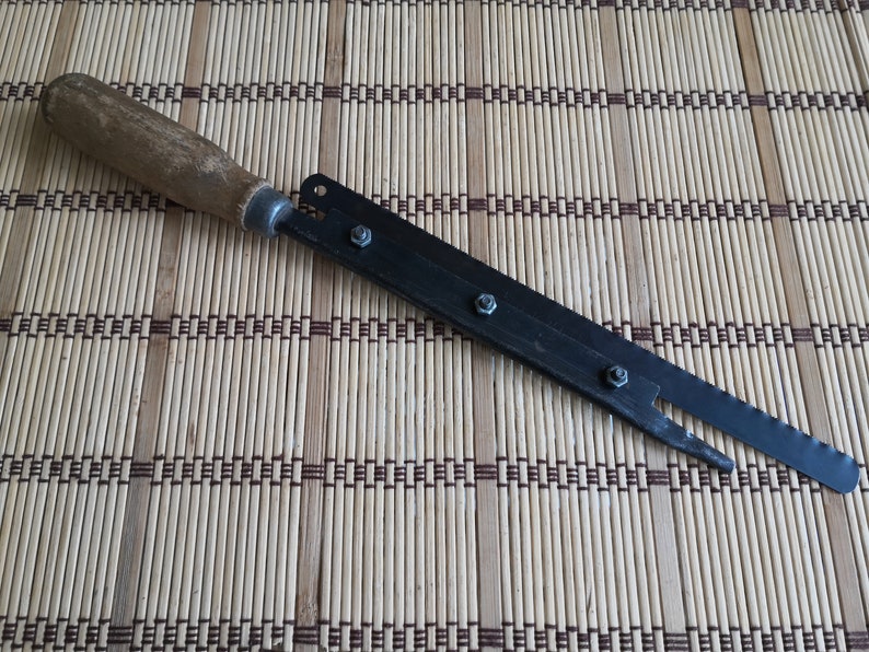 May include: A black metal saw with a wooden handle. The saw has a serrated blade and is attached to the handle with screws.