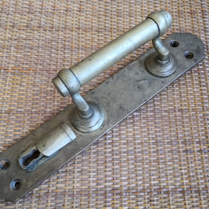 Op de afbeelding: Antiek messing deurbeslag met een lange hendel en een sleutelgat. Het beslag is gemonteerd op een rechthoekige plaat.