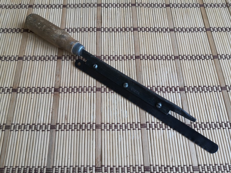 May include: A vintage, black metal, folding utility knife with a wooden handle. The blade is partially open and has a small metal tab with the word "GORDON" printed on it.