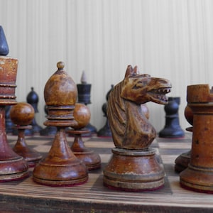 May include: A vintage wooden chess set with brown and black pieces. The pieces are arranged on a wooden chessboard. The knight piece is in the foreground and is carved in the shape of a horse's head.