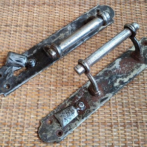 May include: Two antique door latches with a silver finish. One latch is rusty and has a handle. The other latch is black and has a simple design.