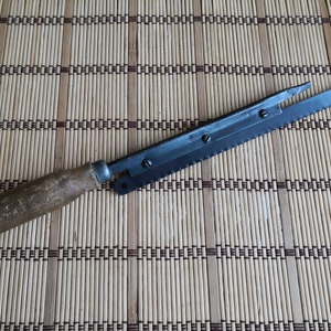 May include: A vintage bread knife with a wooden handle and a serrated blade. The knife is lying on a woven bamboo mat.