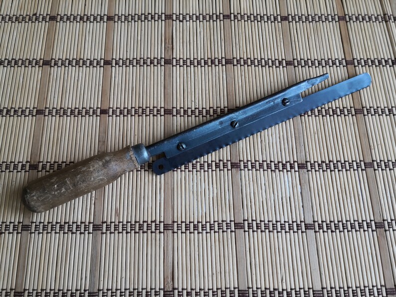 May include: A vintage bread knife with a wooden handle and a serrated blade. The knife is lying on a woven bamboo mat.