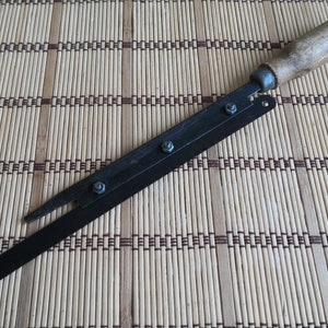 May include: A black metal knife with a wooden handle. The blade is attached to the handle with screws. The knife is lying on a woven bamboo mat.