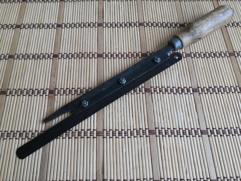May include: A black metal knife with a wooden handle. The blade is attached to the handle with screws. The knife is lying on a woven bamboo mat.