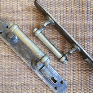 Może przedstawiać: Dwa antyczne mosiężne klamki do drzwi z dziurką od klucza i ozdobnym wzorem. Klamki znajdują się na plecionym tle.