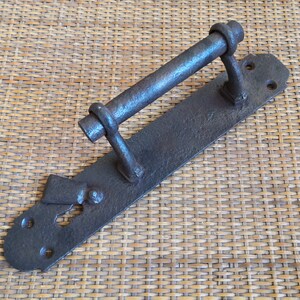 May include: Antique iron door handle with a long, straight bar and a keyhole. The handle is attached to a rectangular plate with decorative details.
