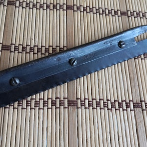 May include: A black metal saw blade with a serrated edge and a small handle. The blade has four screws and the text "2165K" printed on it.