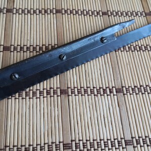 May include: A close-up of a metal saw blade with a handle. The blade has a serrated edge and a small hole near the handle. The blade is marked with the number "2467".